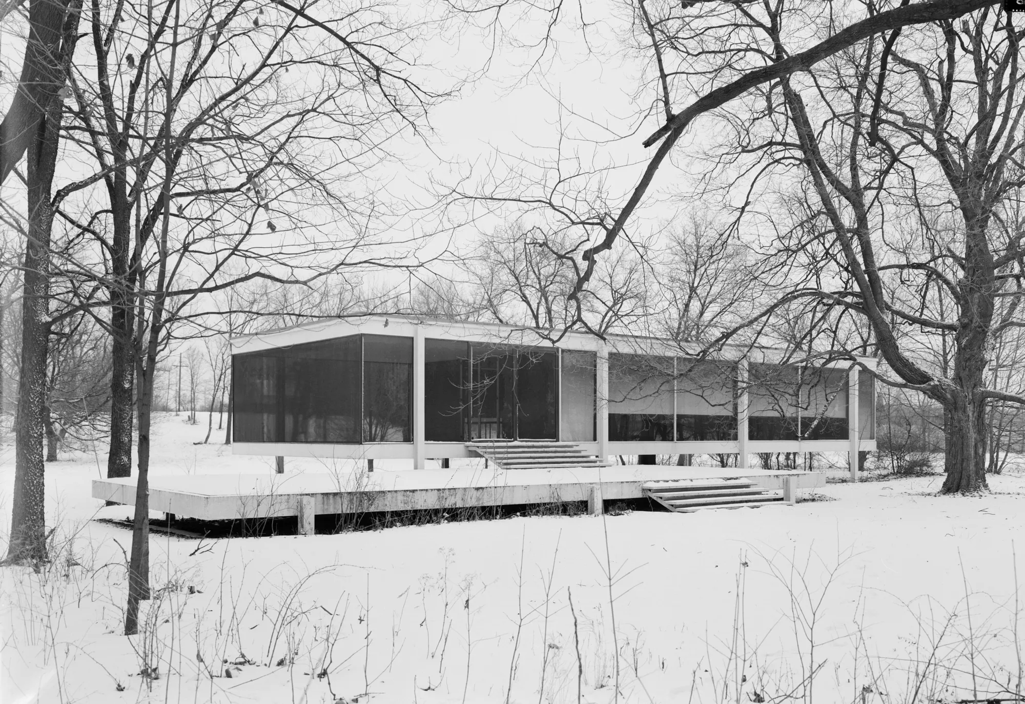 The Farnsworth House seen from the southwest, a low glass and steel pavilion raised on columns in a meadow.