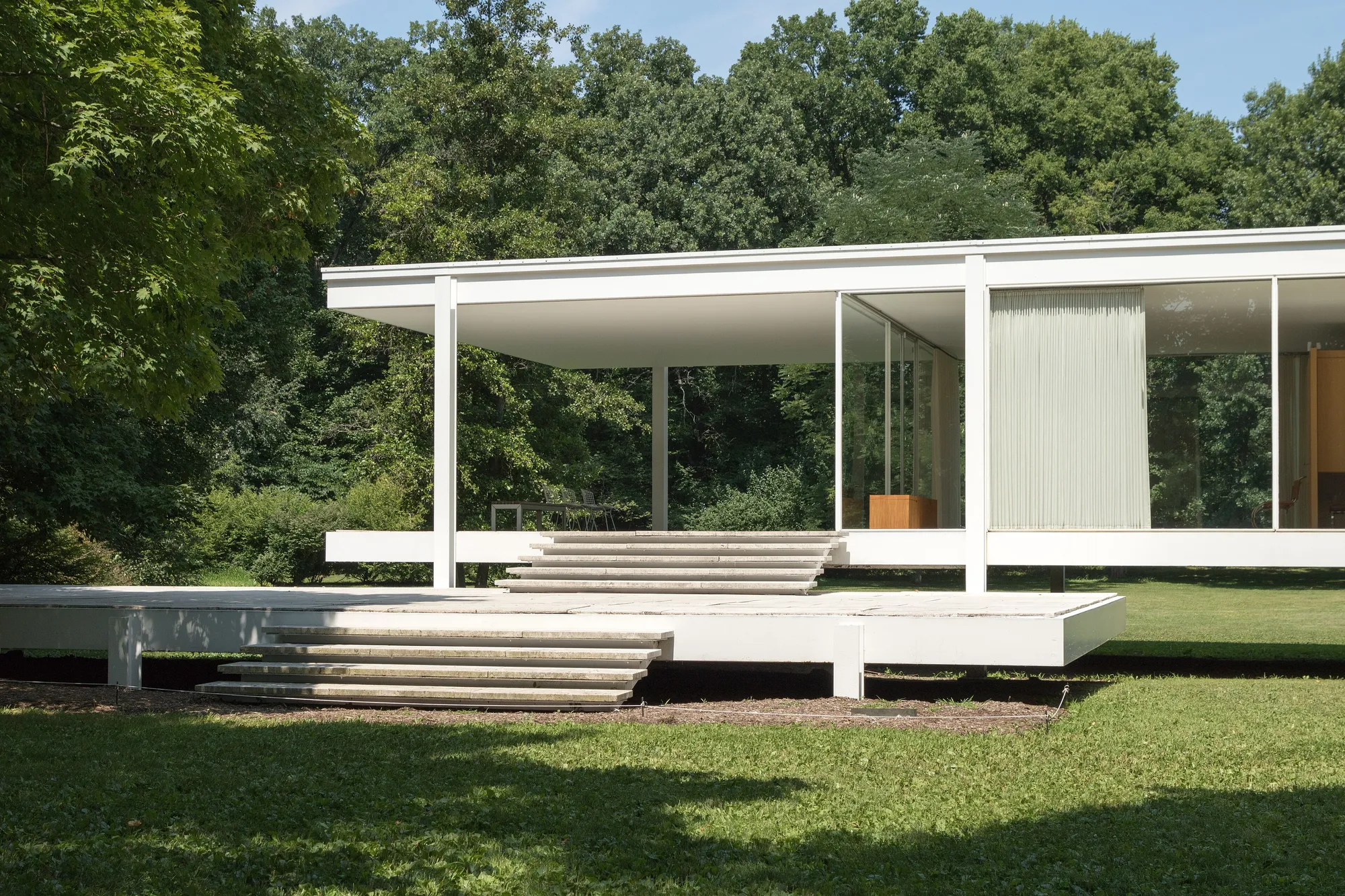 The glass walls of the Farnsworth House and its travertine terrace, seen from the lawn in summer.
