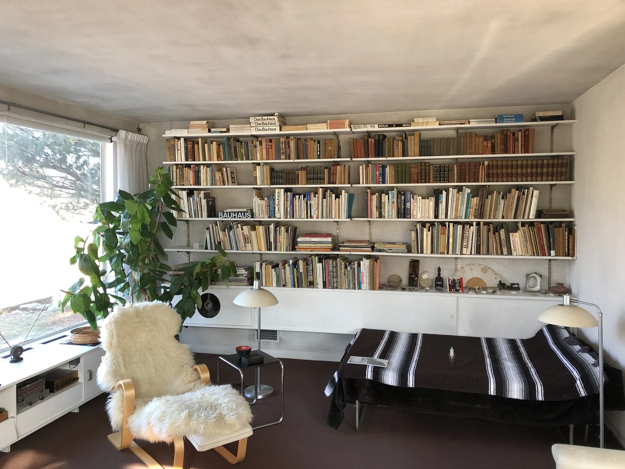 A living room with built-in bookshelves, a sheepskin-covered chair and a striped daybed.