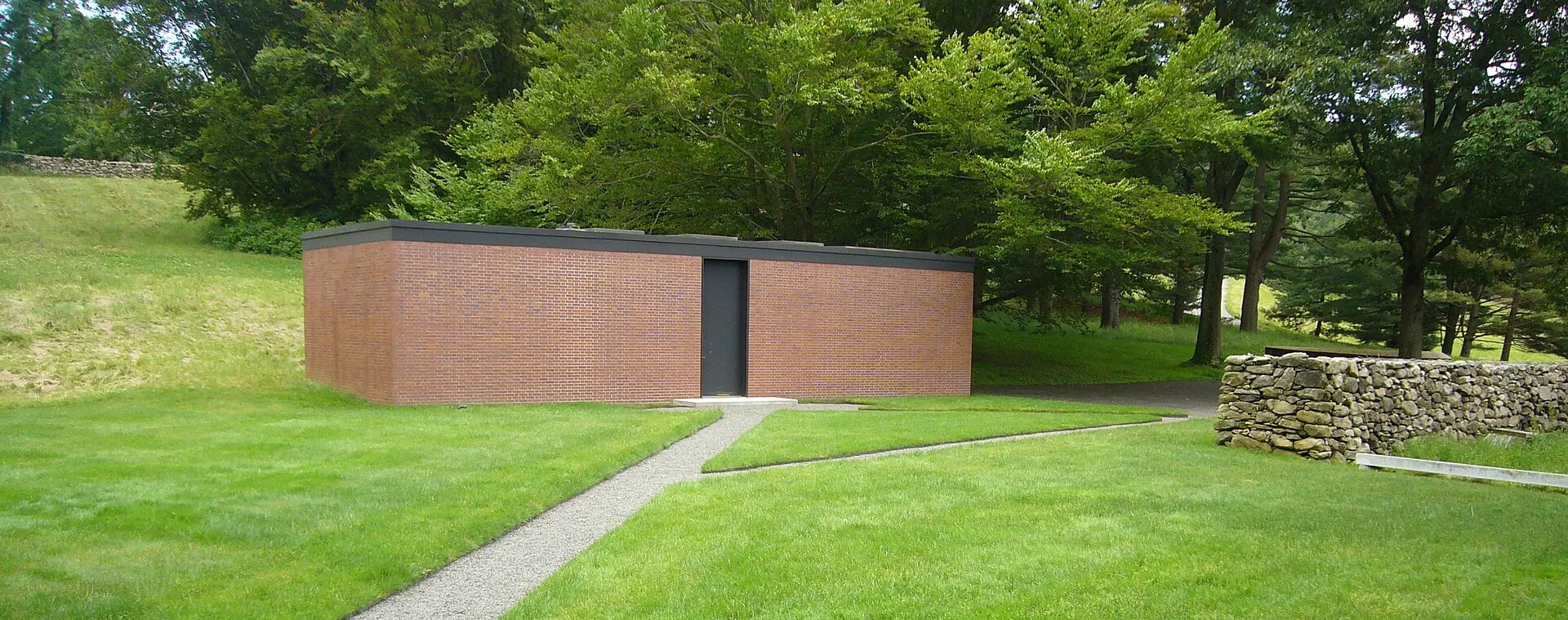 The Brick House on the Glass House estate, a low brick volume with a single dark door, seen from the lawn.