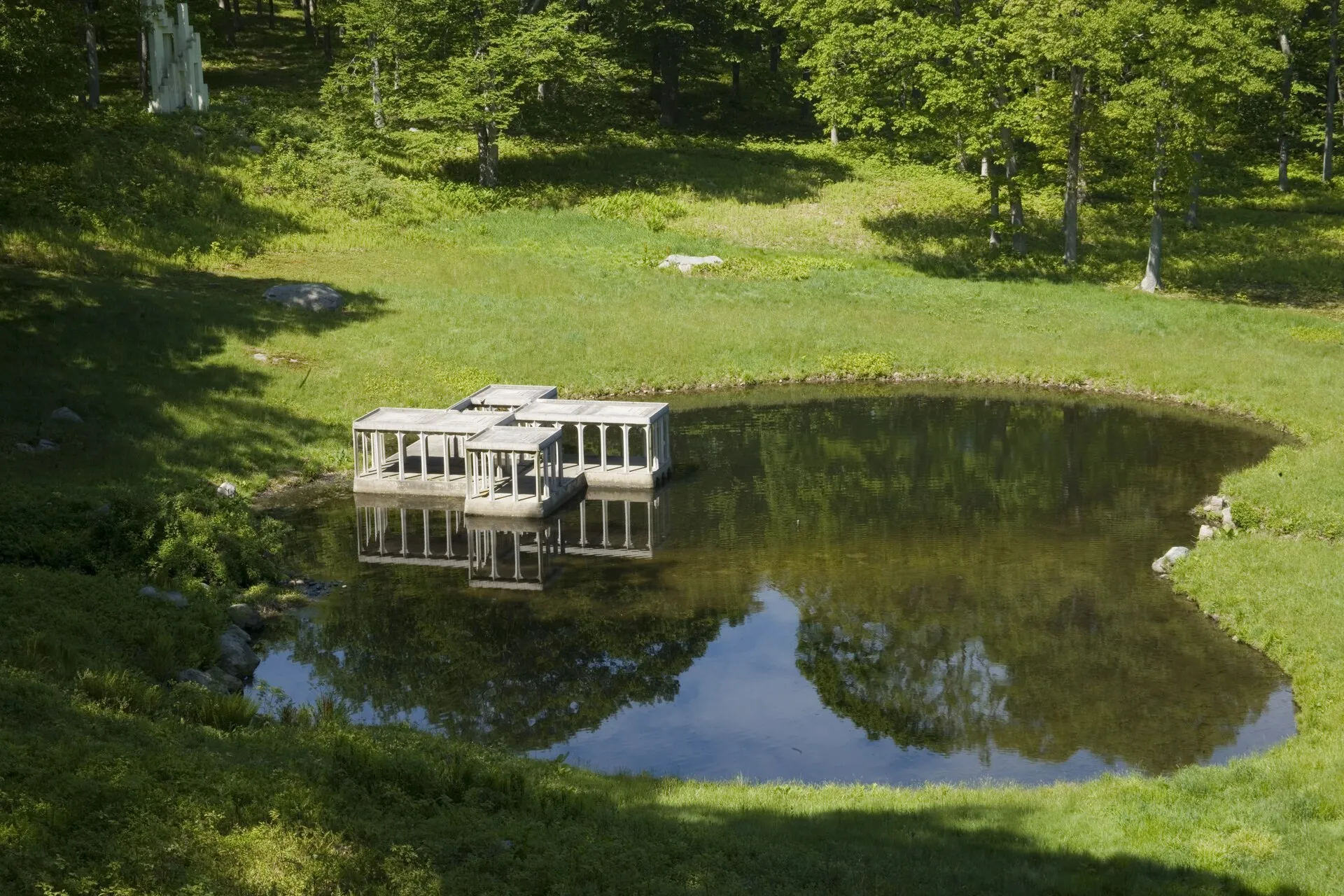 The small concrete Pavilion in the Pond, a row of arches at the water’s edge with a sculpture at the left.