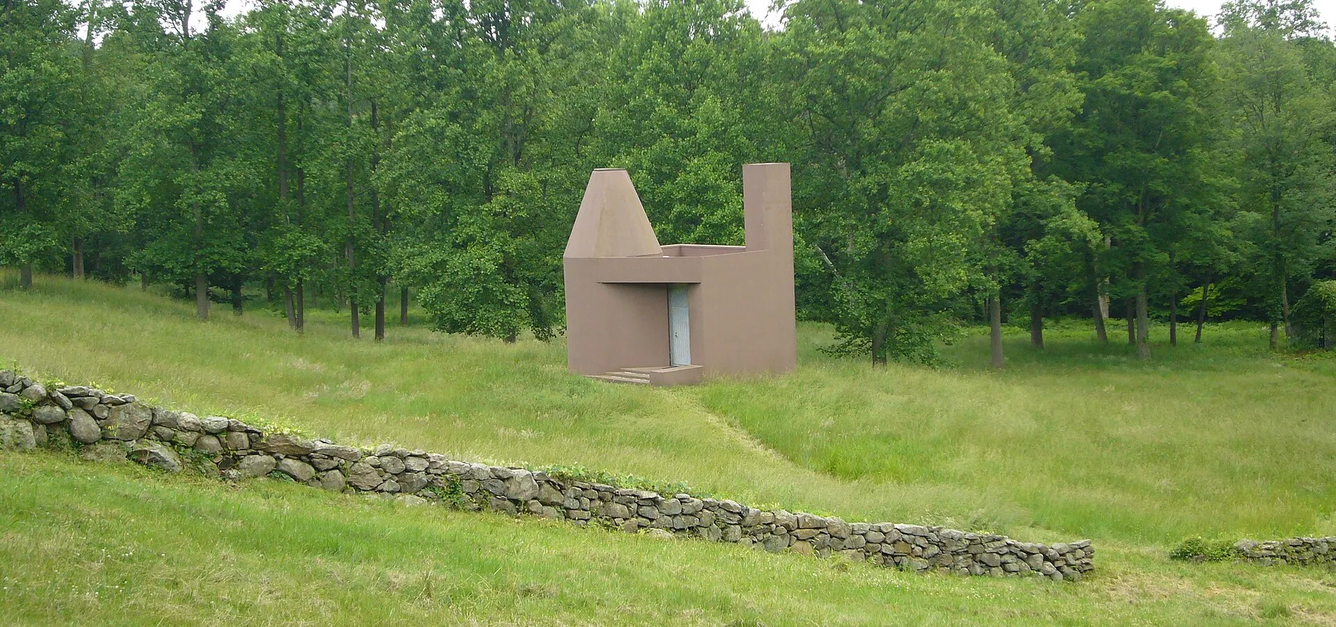 A small brown stucco building with a conical dome standing in tall grass.