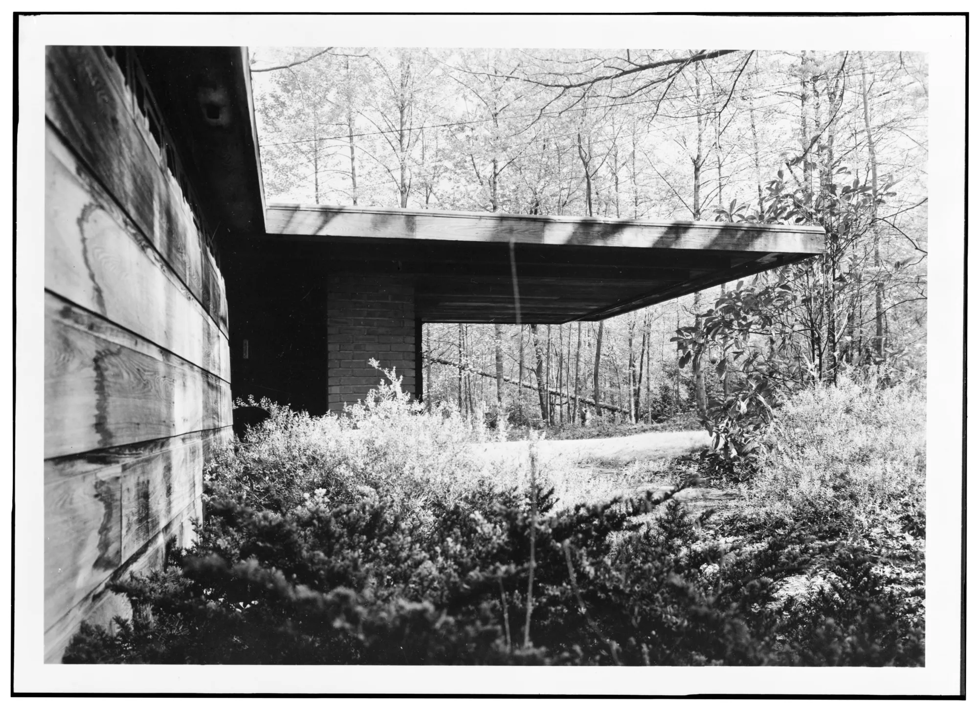 A low house with a flat roof and a carport, seen from the west side.